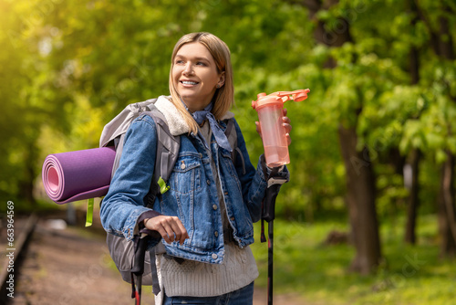 Blonde young woman with a pink bottle in hands in the park