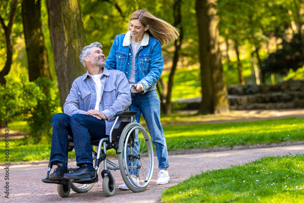 Woman rolling a wheelchair with her husband in the park and both looking happy Woman rolling a wheelchair with her husband in the park and both looking happy