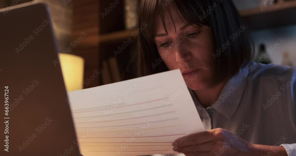 Woman is captured in the midst of work, surrounded by papers and focused on laptop. Her eyes reflect concentration, and hands move swiftly between documents and keyboard. Woman is captured in the midst of work, surrounded by papers and focused on laptop. Her eyes reflect concentration, and hands move swiftly between documents and keyboard.