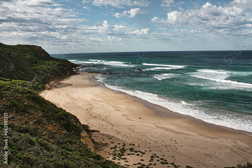 A breathtaking sight on the Great Ocean Road in the state of Victoria, Australia. Cliffs rise into the blue sky, surrounded by lush vegetation. The sun beams down on the calm blue water while a surfer © Erik