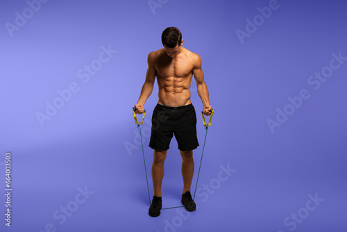 Full length image of a man with an athletic and fit body, posing in the studio with a bare torso, showing six abs pack, isolated on the violet background.