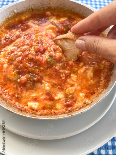 dipping bread slice into delicious scrambled eggs known as menemen in Turkish photo