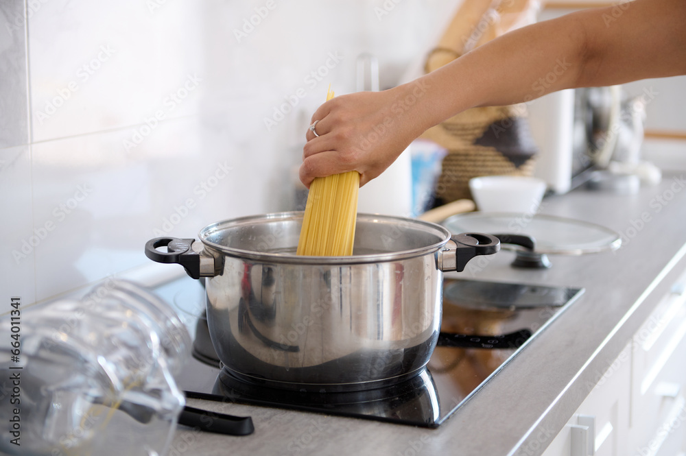 Close-up housewife's hand taking off spaghetti from a container while cooking dinner in the home kitchen Close-up housewife's hand taking off spaghetti from a container while cooking dinner in the home kitchen