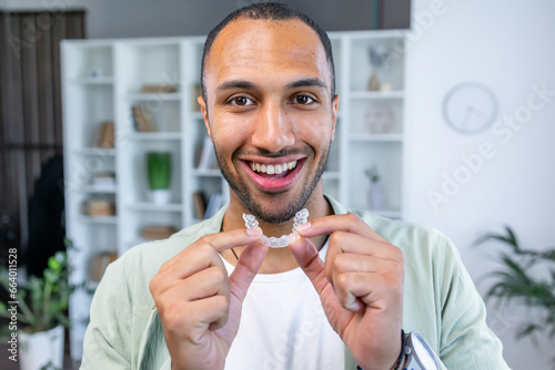 Adult man putting transparent braces for dental correction. holding invisible orthodontic retainer and aligner. Plastic braces dentistry to straighten teeth