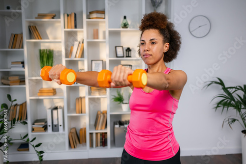 Healthy young woman doing exercises with dumbbells at home. Fit young female doing weights workout indoors in living room.