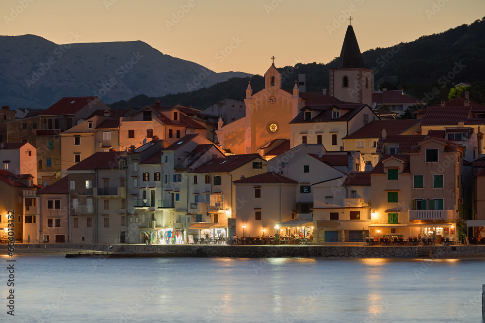 Evening cityscape of the town of Baska on the island of Krk in Croatia. The old town with a promenade by the port. A tourist resort located on the Adriatic Sea with mountains in the background