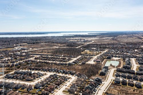 Aerial view of Barrie, Ontario, highlighting dense residential areas adjacent to the expansive, icy expanse of Lake Simcoe. The urban landscape showcases modern homes and infrastructure against a sere © contentzilla