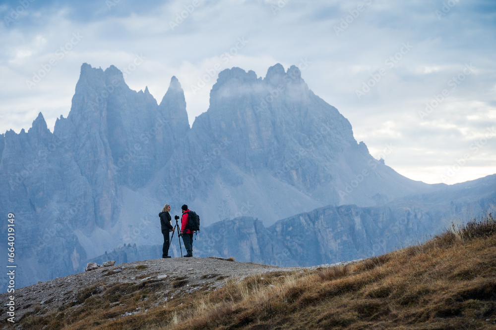 Two landscape photographers talking in front of impressive rock wall of mountains, Italy, Europe