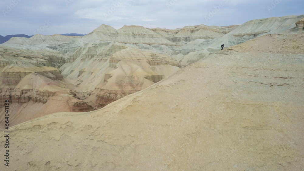 Colorful high mountains and a canyon made of clay. A large gorge with different rocks and different colors. Red, orange, white and yellow flowers of the walls of the rocks. A tourist walks. Aktau Colorful high mountains and a canyon made of clay. A large gorge with different rocks and different colors. Red, orange, white and yellow flowers of the walls of the rocks. A tourist walks. Aktau