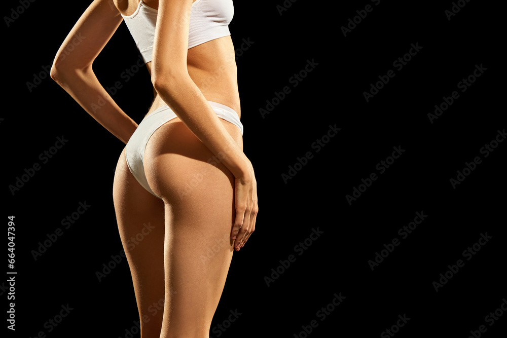 Cropped image of fit, smooth female body, buttocks in white underwear against black studio background. Anti cellulite care. Concept of natural beauty, body and skin care, health, sport, wellness.