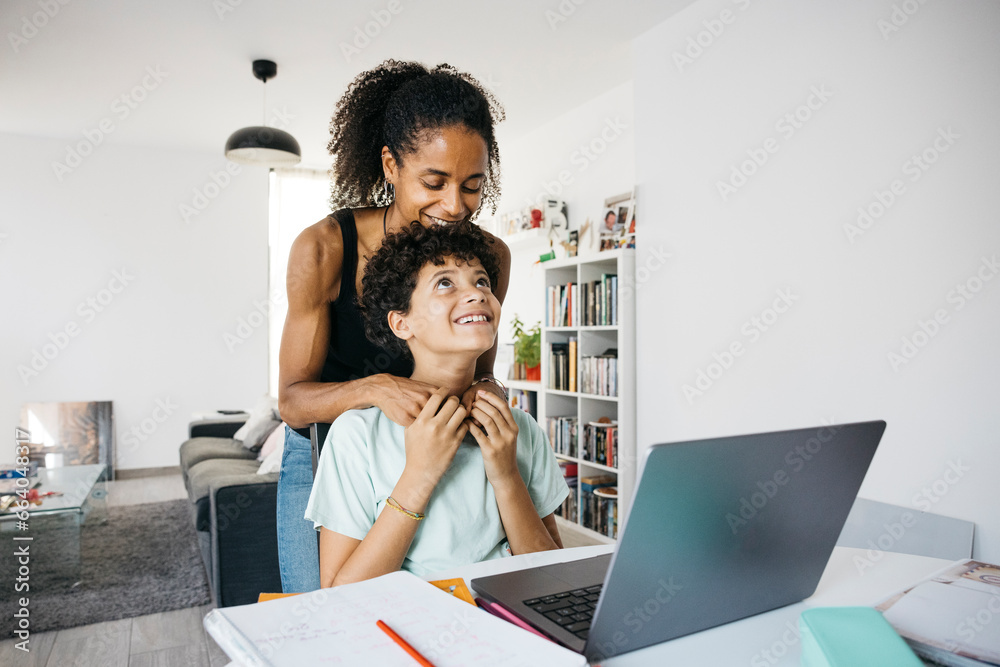 Cheerful woman helping her smiling daughter doing homework. Happy mother assisting her daughter with school homework in living room. Cheerful woman helping her smiling daughter doing homework. Happy mother assisting her daughter with school homework in living room.