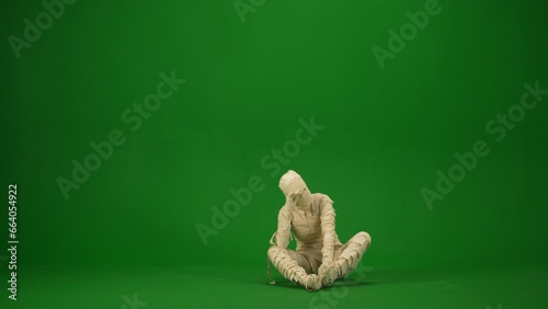 A tired or frustrated mummy sits on the floor and holds his head. Green screen isolated chroma key. Mock up, workspace, advertisement. Full length. © kinomaster