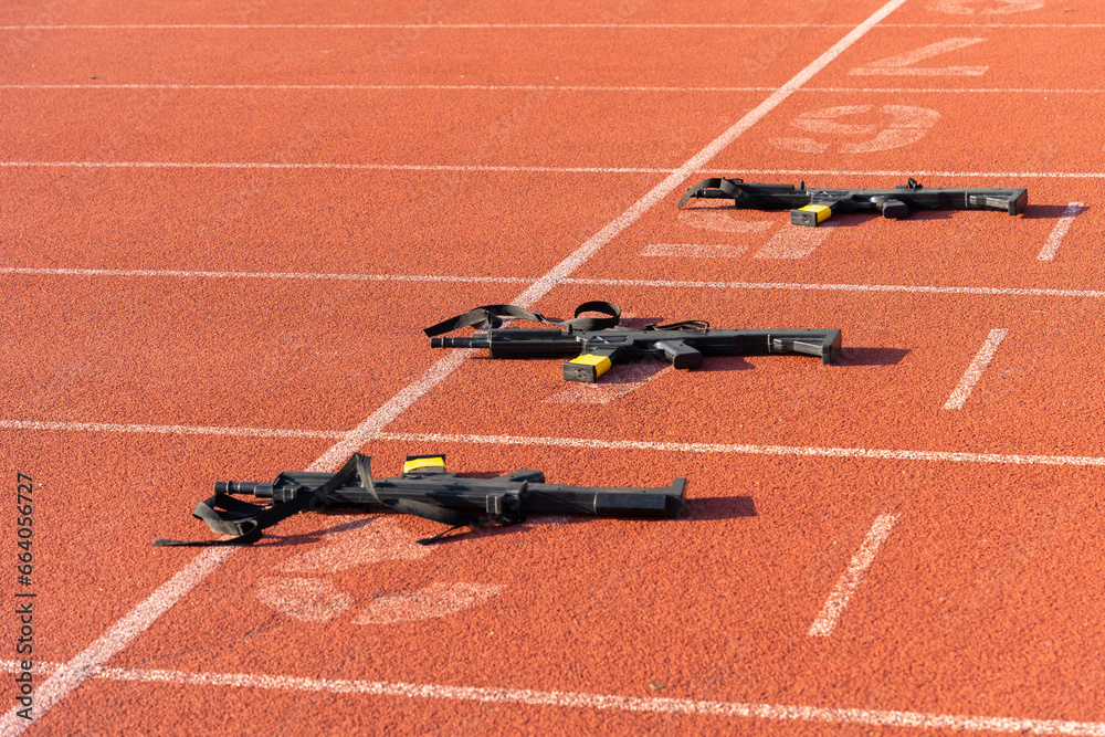 Black practice weapons on the dotted starting line of an orange running track