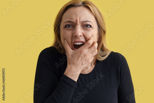Scared mature woman on yellow background, closeup