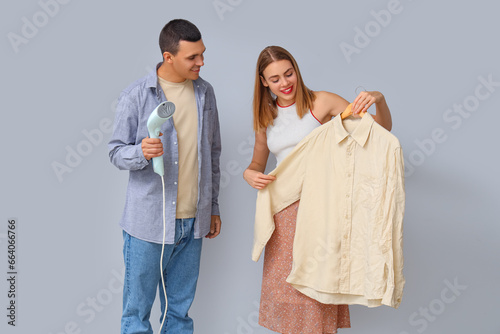 Young couple with steamer and shirt on light background photo