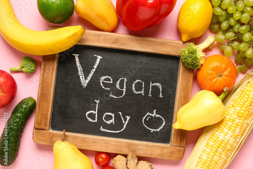 Chalkboard with word VEGAN DAY, fresh vegetables and fruits on pink background