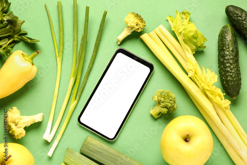 Mobile phone with vegetables and fruits on green background. World Vegan Day concept