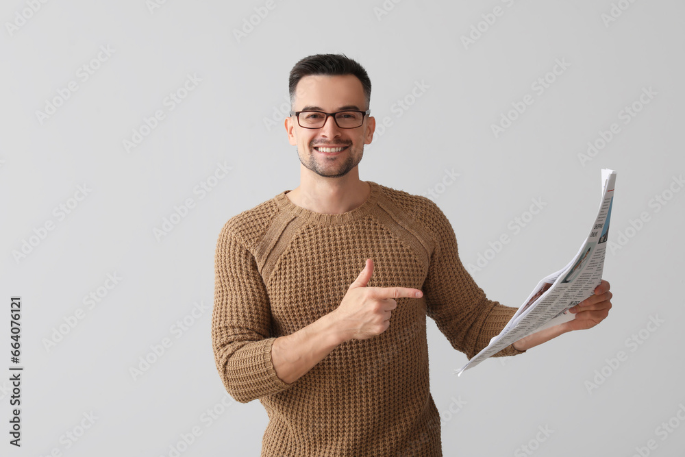 Happy young man pointing at newspaper on light background - obrazy, fototapety, plakaty 