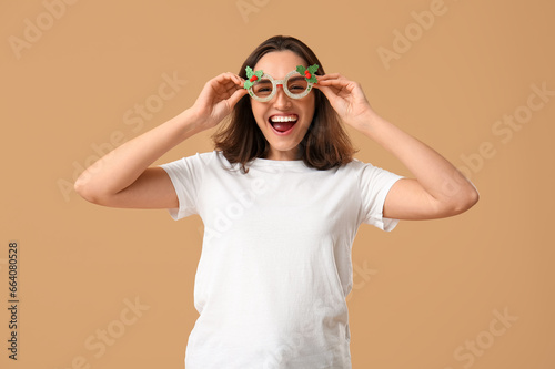 Beautiful young woman in pajamas with Christmas glasses on brown background © Pixel-Shot