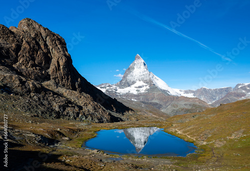 The iconic Matterhorn mountain, located in Zermatt, Switzerland, is beautifully reflected in the tranquil waters of Riffelsee on a clear and sunny autumn day, creating a mesmerizing alpine vista