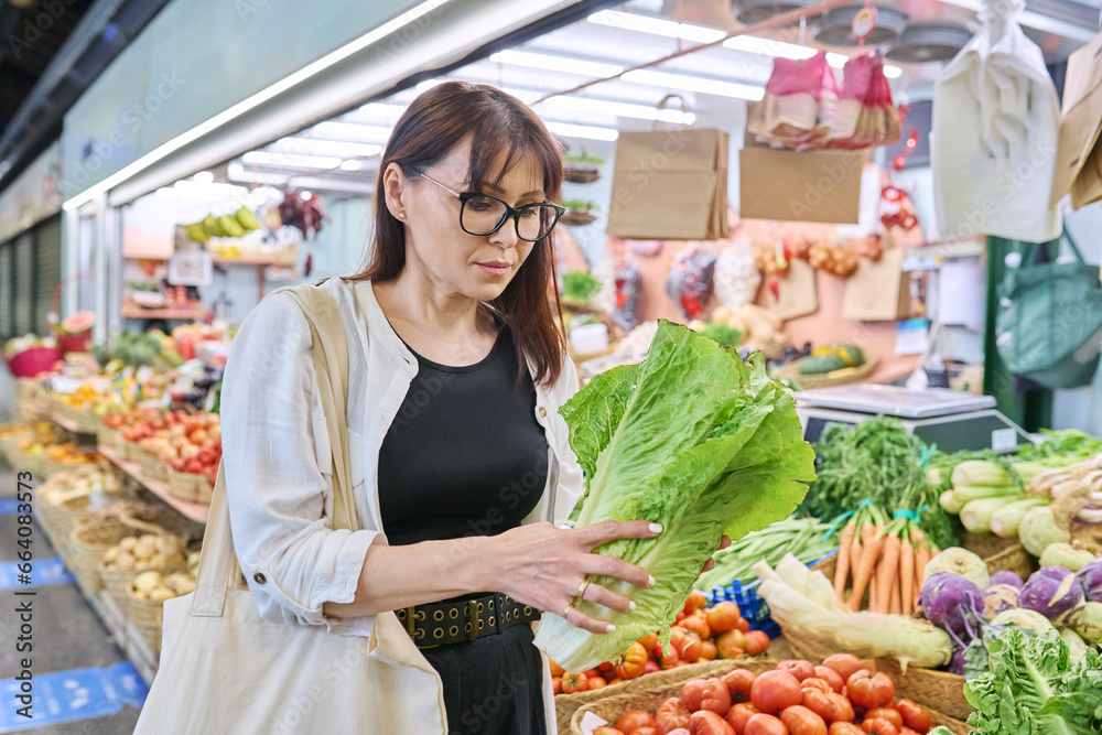 Obraz premium Adult woman choosing buying lettuce bushes at farmers market