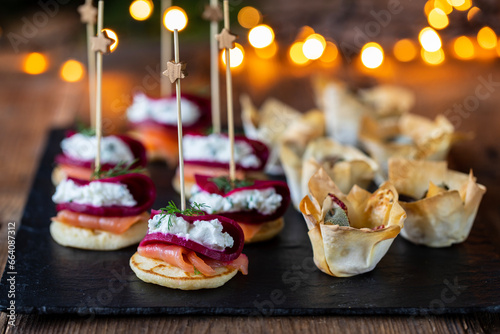 Fotografia Christmas canapes with blinis with salmon, beetroot and goat cheese and filo pas