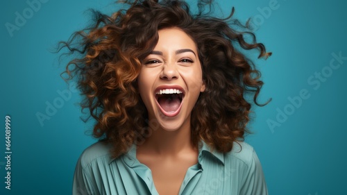 Happy woman with curly brown hair smiling broadly on blue background