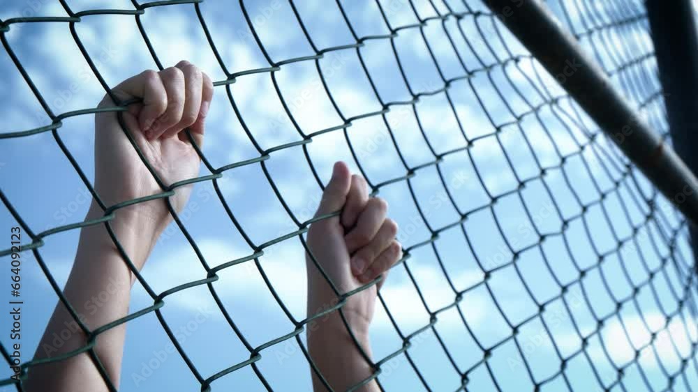 Child's hands on the wire mesh of the refugee camp.