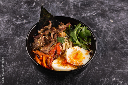 Rice bowl with beef, noodles, egg and vegetables on a dark background