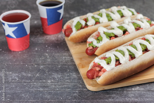 complete Italian: on wooden board, bowls with moztaza, mayonnaise and ketchup. vianesa, palta on hot dog bun, patriotic holiday glasses, with Chilean flag Left copy space. Typical Chilean food concept