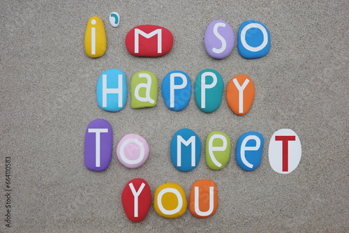 I am so happy to meet you, creative message composed with multi colored stone letters over beach sand