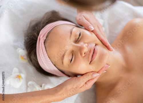 Young woman client getting relaxing facial massage in massage room