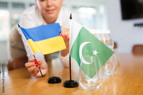 Young woman in business clothes puts flags of Ukraine and Pakistan on negotiating table in office