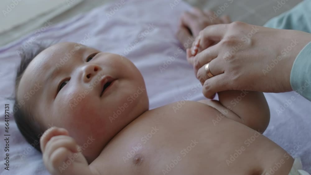 Unrecognizable mom stroking her infant son on belly while her lying on his back and looking around with curiousness Unrecognizable mom stroking her infant son on belly while her lying on his back and looking around with curiousness