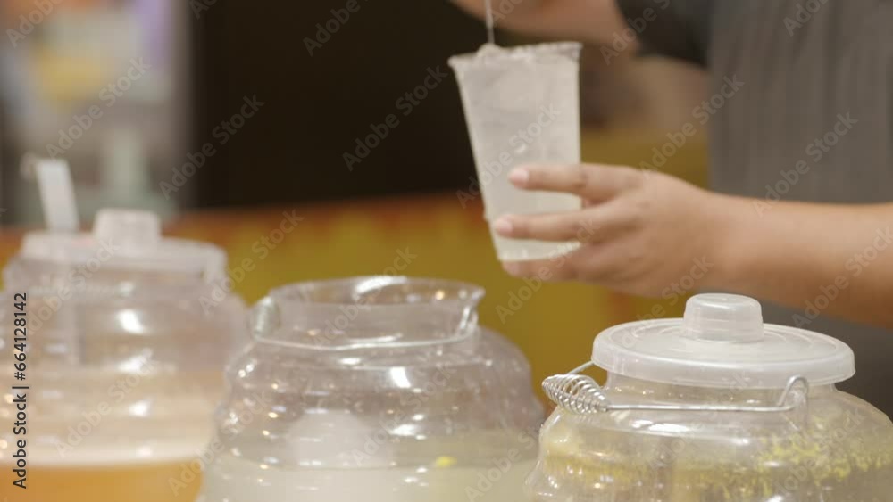 This close up video shows anonymous hands of a vendor serving agua frescas juices with a ladle spoon into cups.