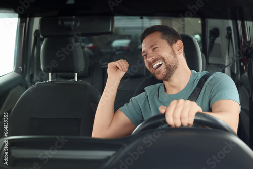 Listening to radio. Handsome man enjoying music in car, view through windshield