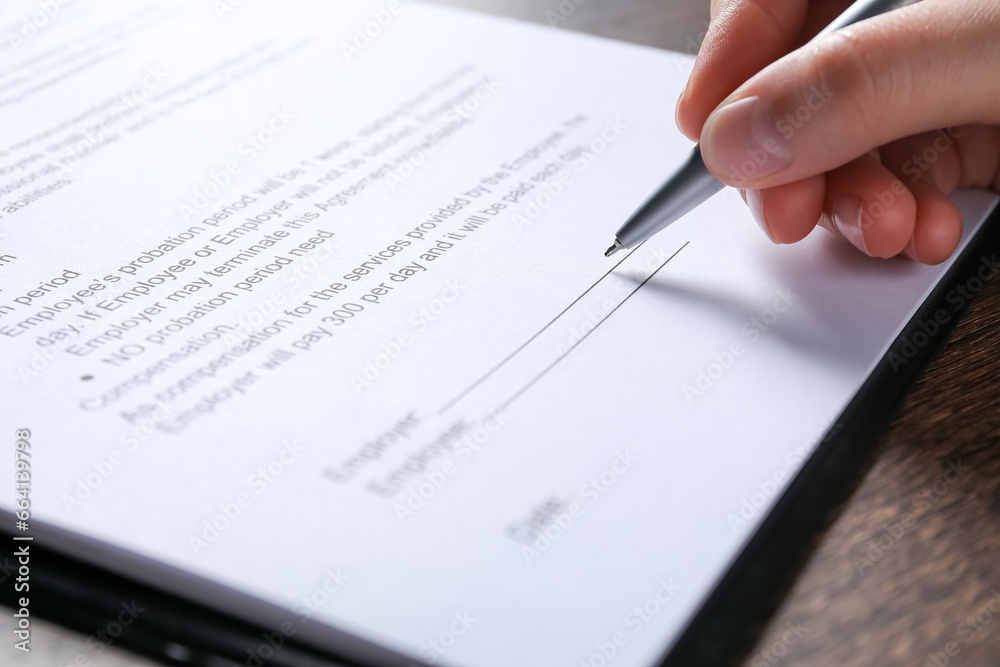 Woman signing document with pen at wooden table, closeup Woman signing document with pen at wooden table, closeup