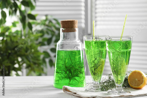 Homemade refreshing tarragon drink, sprigs and lemon on white wooden table, space for text photo