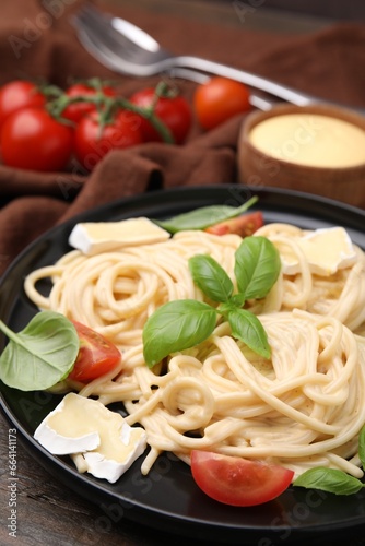 Delicious pasta with brie cheese, tomatoes and basil leaves on table, closeup