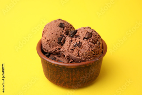 Bowl of tasty ice cream with chocolate chunks on yellow background, closeup