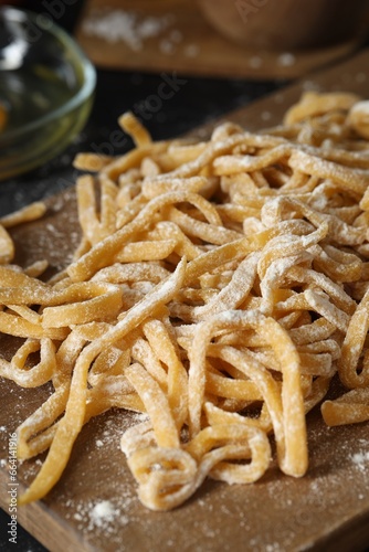Board with homemade pasta and flour on dark table, closeup