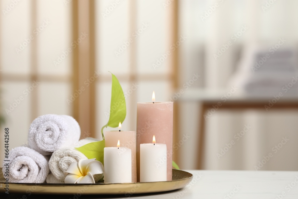 Spa composition. Burning candles, plumeria flower, green leaves and towels on white table indoors, space for text