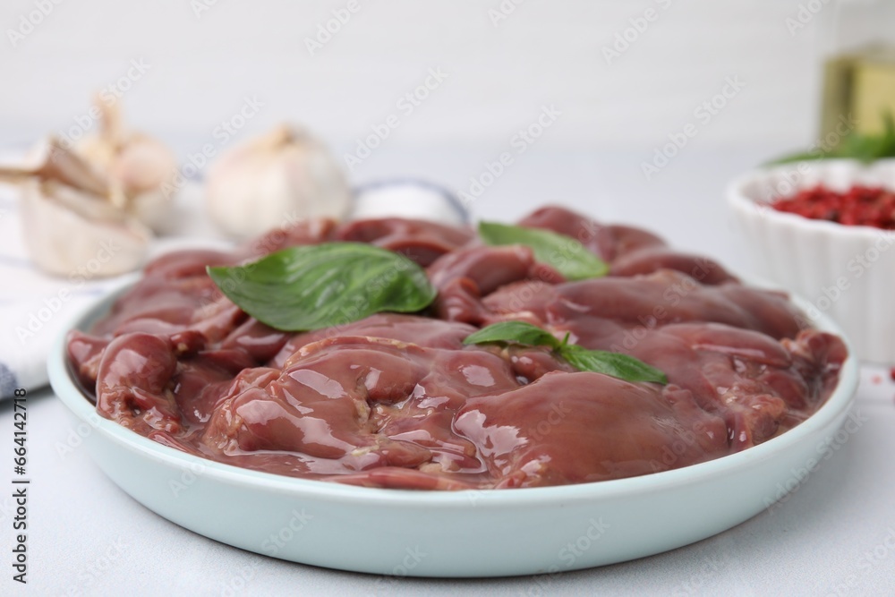 Plate of raw chicken liver with basil on white table, closeup