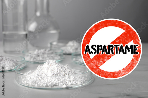 Prohibition sign with word Aspartame symbolizing restriction on use of sugar substitute. Artificial sweetener in Petri dishes on gray table