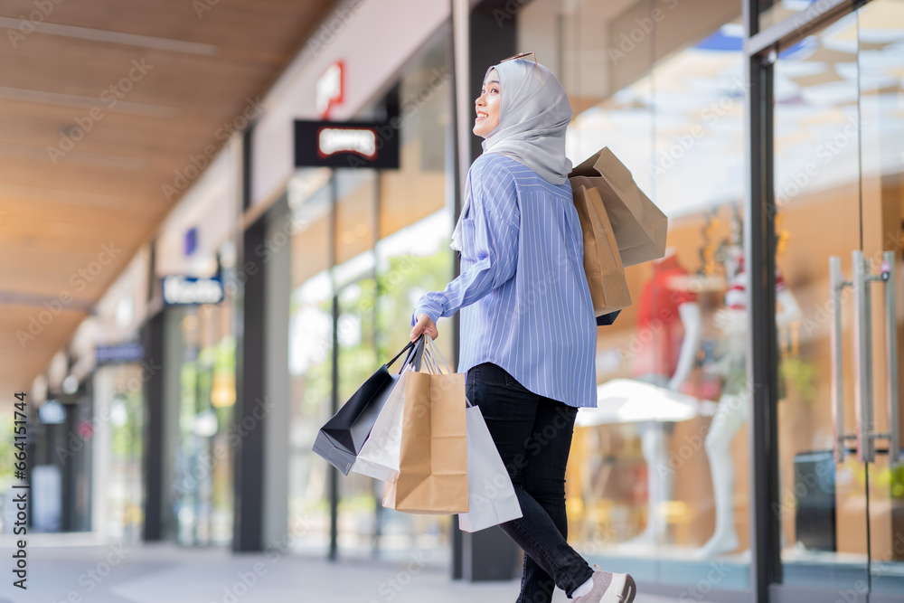 An Asian Muslim woman is carrying a bag of goods that she has been shopping for and buying a lot of products with happy, happy faces.