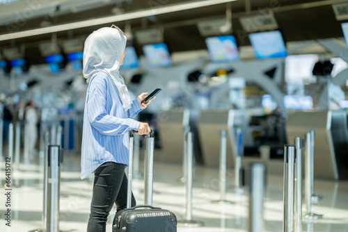 An Asian Muslim wearing a blue hijab is preparing for a vacation and she is at the international airport. She is waiting for her friends, Muslim travelers, holiday concept.