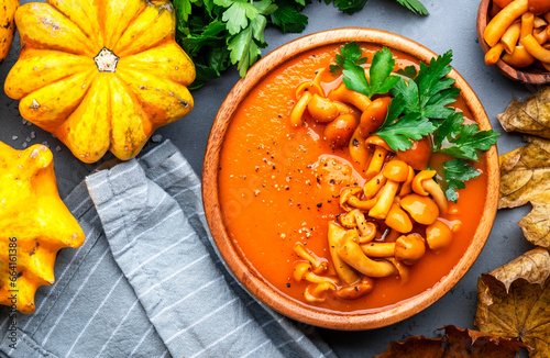 Vegan pumpkin soup puree with mushrooms, pepper and parsley. Winter or autumn healthy vegetarian slow food. Ceramic bowl on gray table background. Top view