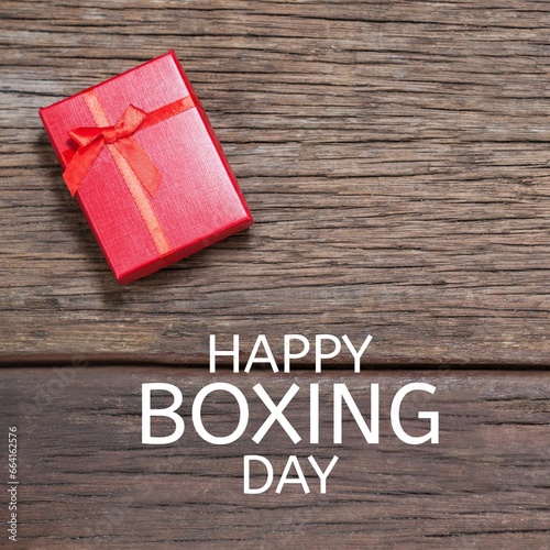 Composite of happy boxing day text over red gift box on wooden table