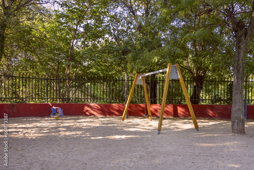 swing with chains on a playground with wooden arms and sand on the ground