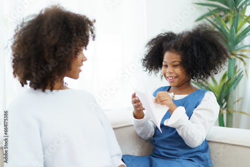 Lovely cute little girl gives mother her drawing post card in the international Mother's Day, American - African black ethnic family portrait. International Mother's Day concept.